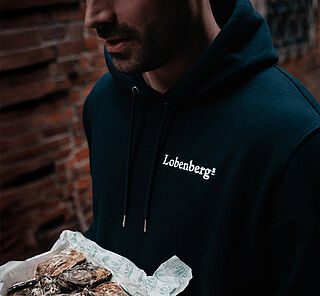Eine Person im Lobenbergs Hoodie hält eine Box mit Austern