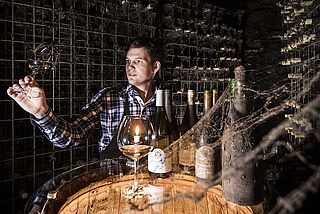 Donatsch Winzer im Keller mit alten Flaschen und probiert Wein