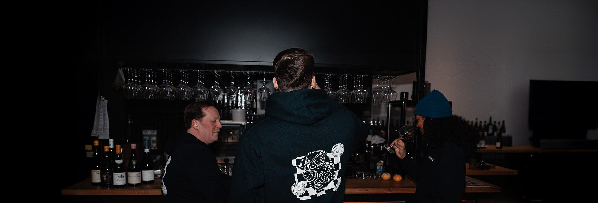 Drei Personen in Lobenbergs Hoodies sitzen an der Bar